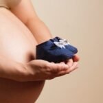 Pregnant woman holding baby shoes to her belly