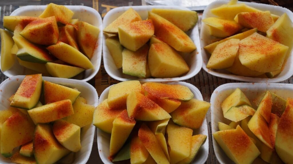 Pieces of cut mango fruit with red chilli and spices on them