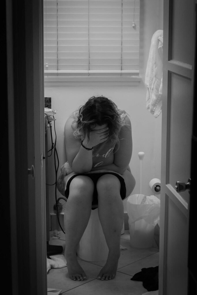 Woman holding her head sitting on the toilet